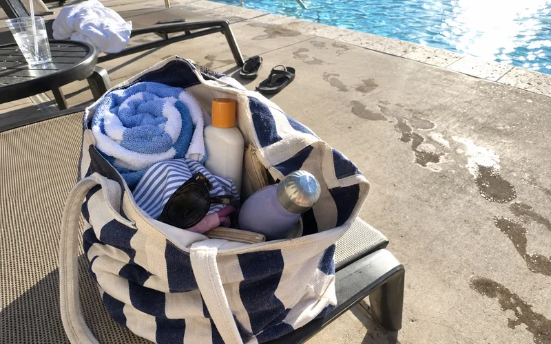 Sunscreen bottle packed in a canvas pool bag on a lounge chair next to a pool