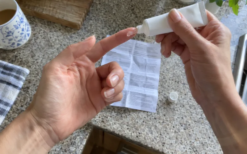 A woman's hands squeezing a small line of prescription redness gel onto a fingertip