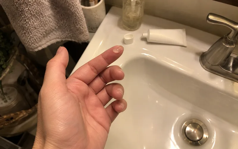 Small dot of retinoid gel on a fingertip over a bathroom sink at night